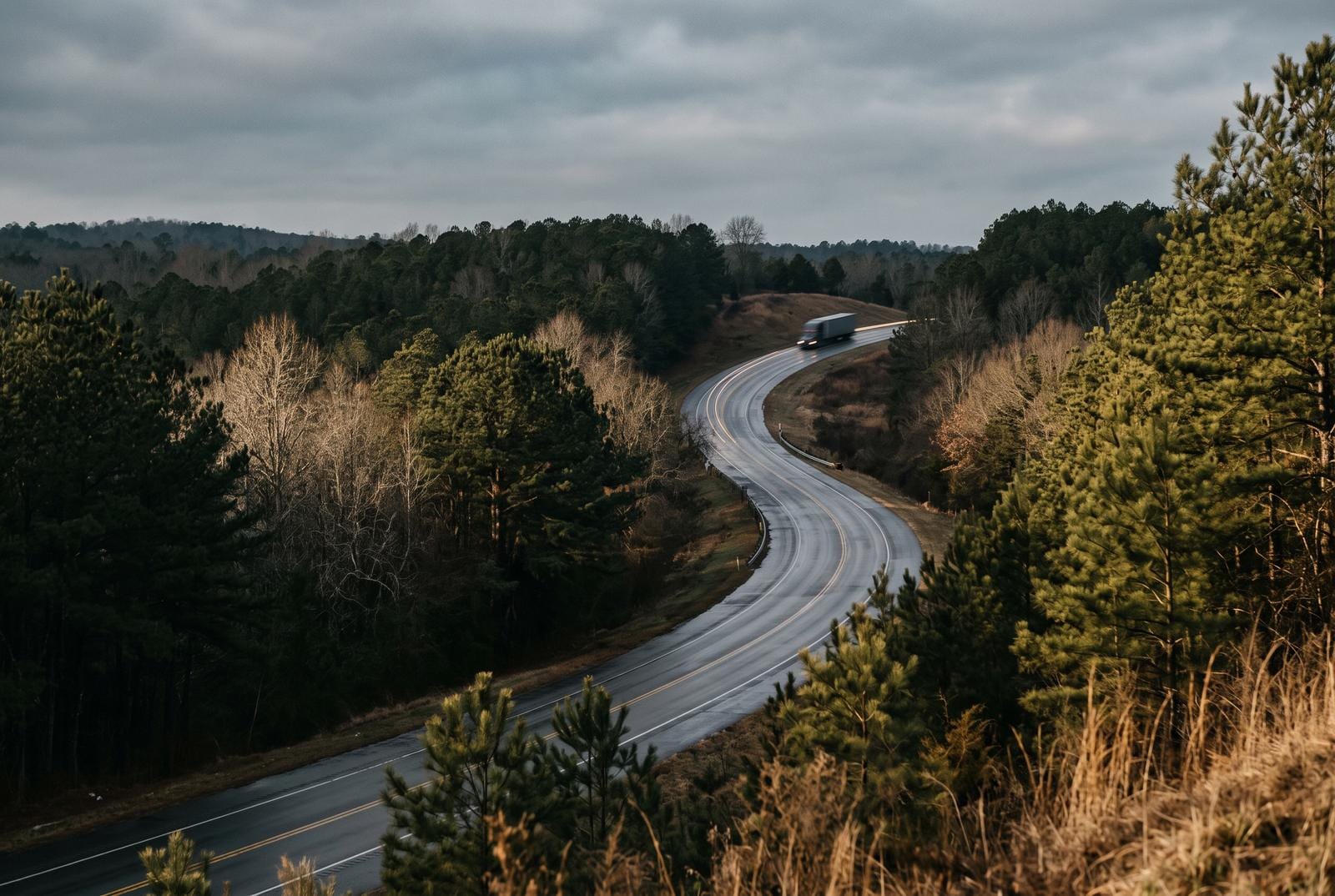 A two-lane state route through low hills with a tractor-trailer on a distant rise