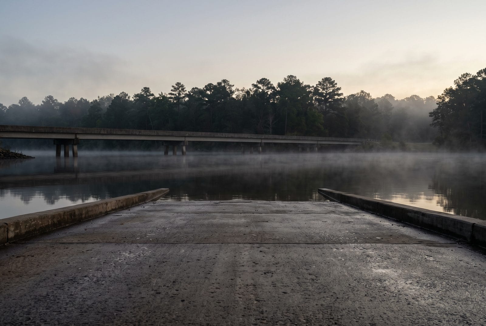 A lake shore with a concrete ramp and a low causeway, mist on the water
